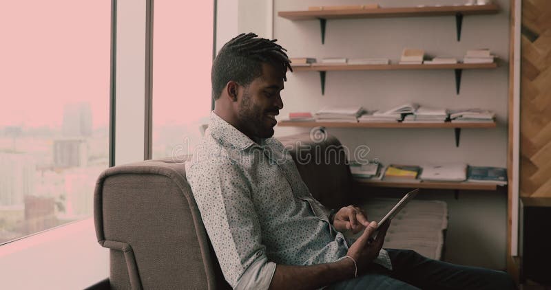 Jeune homme africain heureux détendu en utilisant le comprimé numérique. banque de vidéos