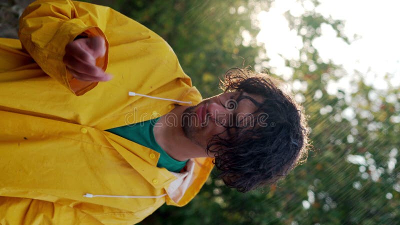 Jeune homme arabe qui apprécie la pluie d'été avec un imperméable jaune banque de vidéos