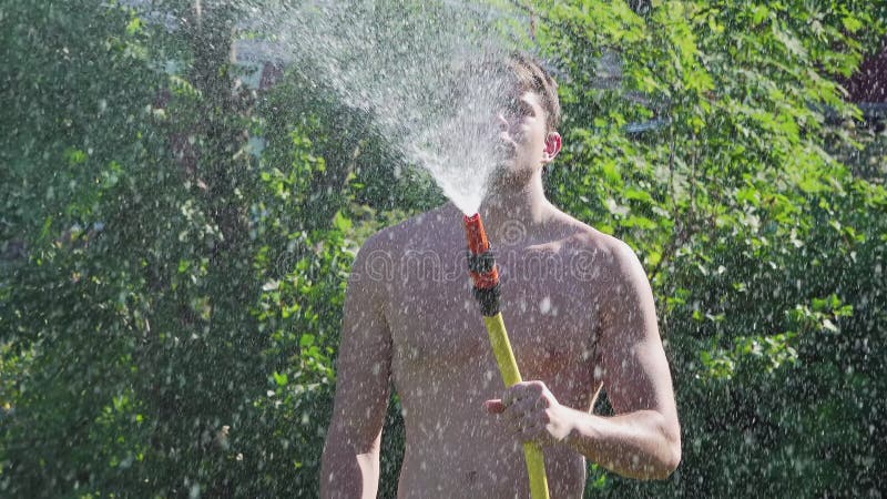 Jeune homme arrosant pelouse et plantes dans le jardin en utilisant l'eau de source d'hosepipe pour une meilleure distribution fer banque de vidéos
