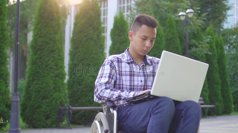 Jeune homme asiatique handicapé en fauteuil roulant avec ordinateur portable slow mo