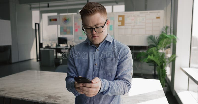 Jeune homme atteint du syndrome de down utilisant un smartphone debout sur le lieu de travail banque de vidéos