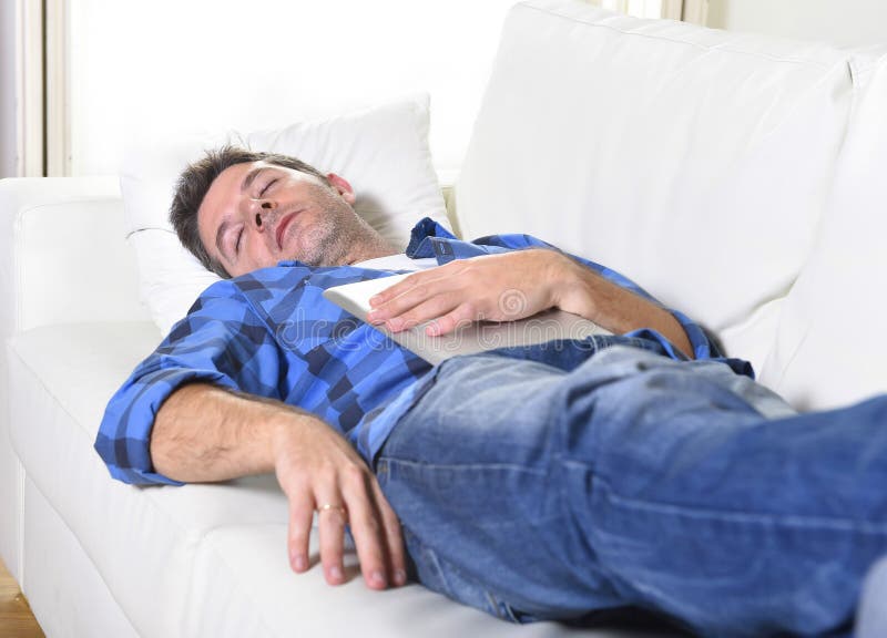 Jeune homme attirant dormant à la maison divan détendant après travail avec la protection numérique de comprimé photographie stock libre de droits