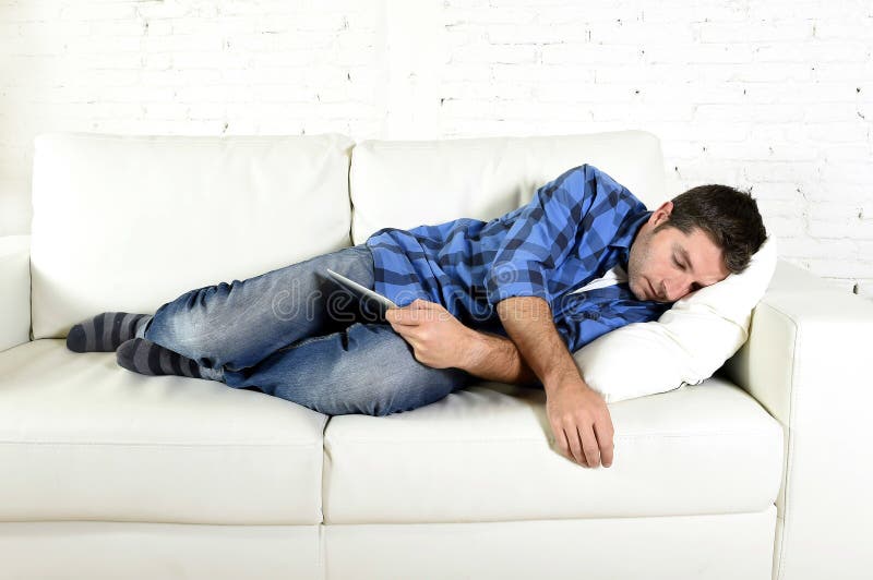 Jeune homme attirant dormant à la maison divan détendant après travail avec la protection numérique de comprimé photo libre de droits