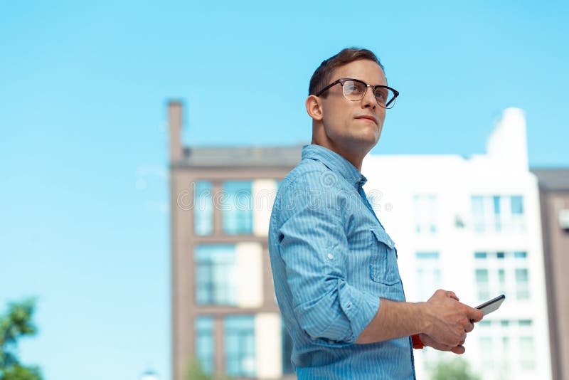 Jeune homme aux cheveux foncés beau marchant près des blocs de ville image stock Jeune homme aux cheveux foncés beau marchant près des blocs de ville image stock