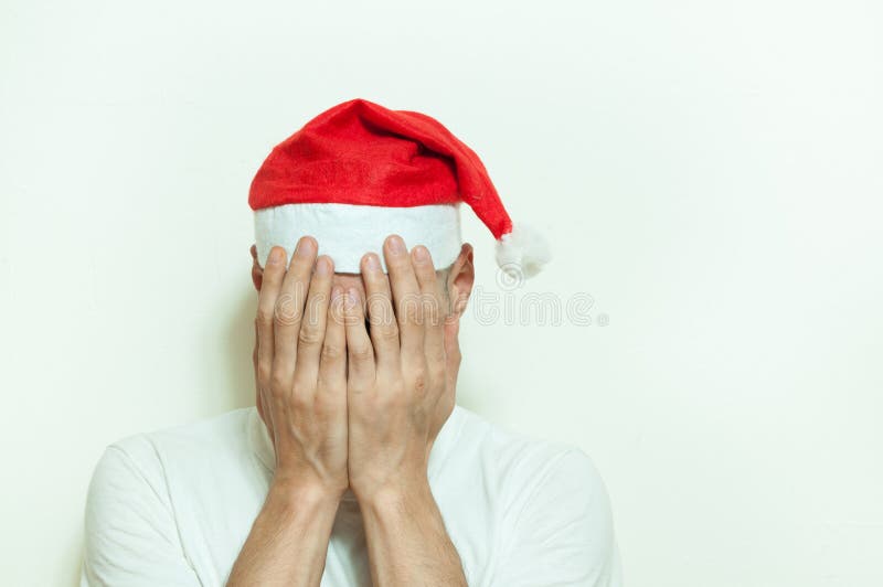 Jeune homme avec la couverture de chapeau de Santa Claus son visage avec ses mains se sentant isolées et tristes dépression pour image stock Jeune homme avec la couverture de chapeau de Santa Claus son visage avec ses mains se sentant isolées et tristes dépression pour image stock