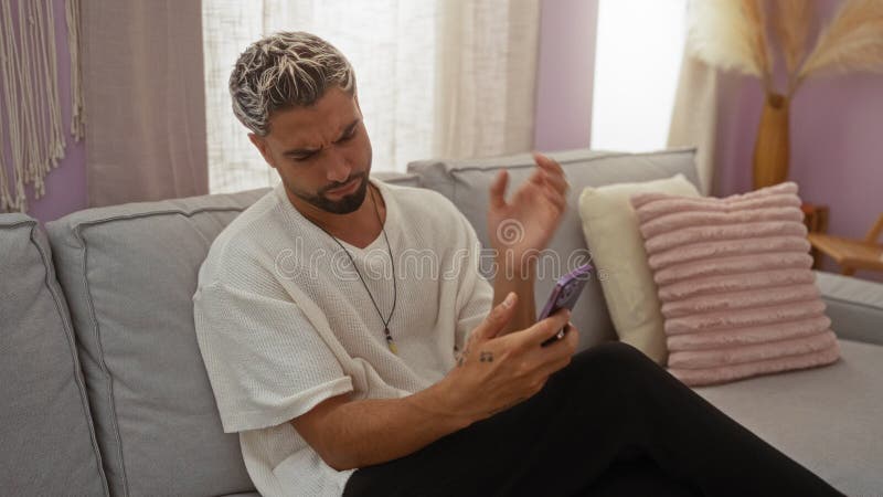 Jeune homme avec une barbe utilisant un téléphone dans un salon semblant frustré par la douleur du cou clips vidéos