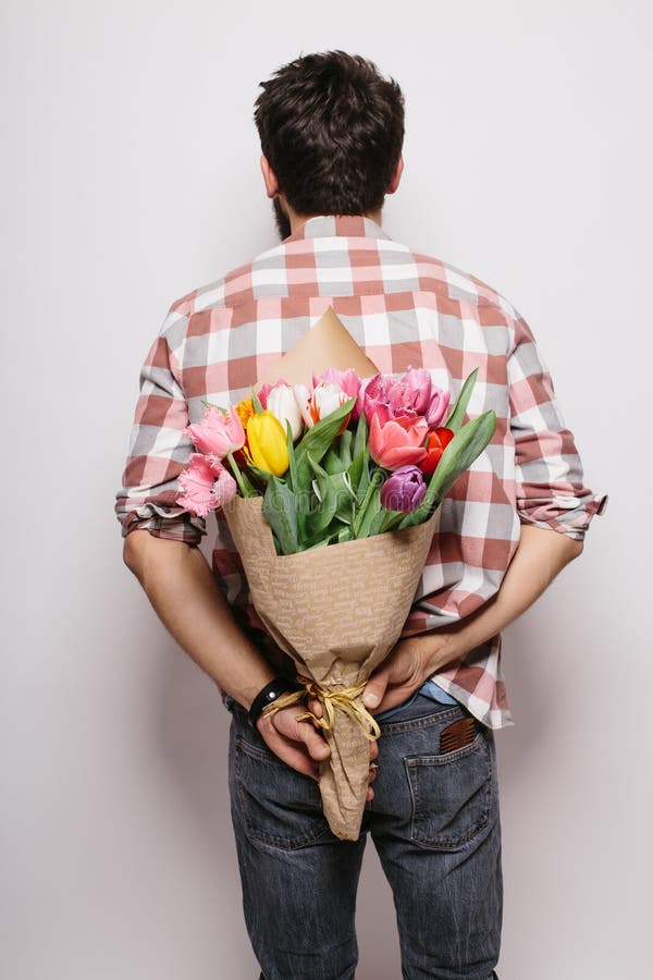 Jeune homme beau arrière avec la barbe et le bouquet gentil des fleurs photographie stock libre de droits Jeune homme beau arrière avec la barbe et le bouquet gentil des fleurs photographie stock libre de droits