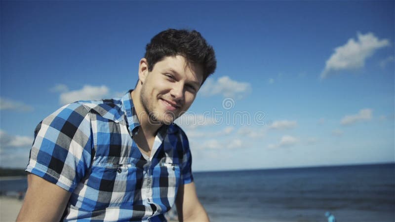 Jeune homme beau dans la chemise à carreaux occasionnelle sur le fond lumineux de plage