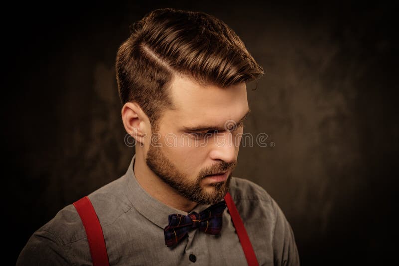 Jeune homme bel avec les bretelles de port de barbe et pose sur le fond foncé photos libres de droits Jeune homme bel avec les bretelles de port de barbe et pose sur le fond foncé photos libres de droits