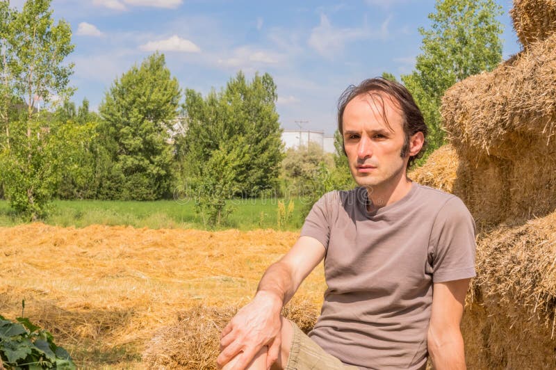 Jeune homme bel se reposant sur des balles de paille un jour ensoleillé image stock Jeune homme bel se reposant sur des balles de paille un jour ensoleillé image stock