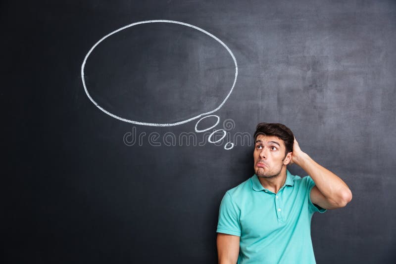 Jeune homme confus réfléchi se tenant et pensant au-dessus du fond de tableau noir images stock Jeune homme confus réfléchi se tenant et pensant au-dessus du fond de tableau noir images stock
