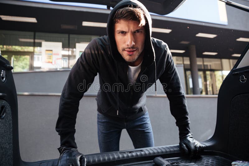 Jeune homme criminel tenant et regardant le tronc de voiture photo stock Jeune homme criminel tenant et regardant le tronc de voiture photo stock