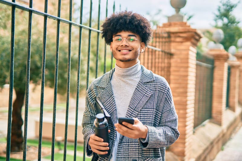 Jeune homme d'affaires africain américain utilisant un smartphone tenant une bouteille d'eau à la ville images libres de droits