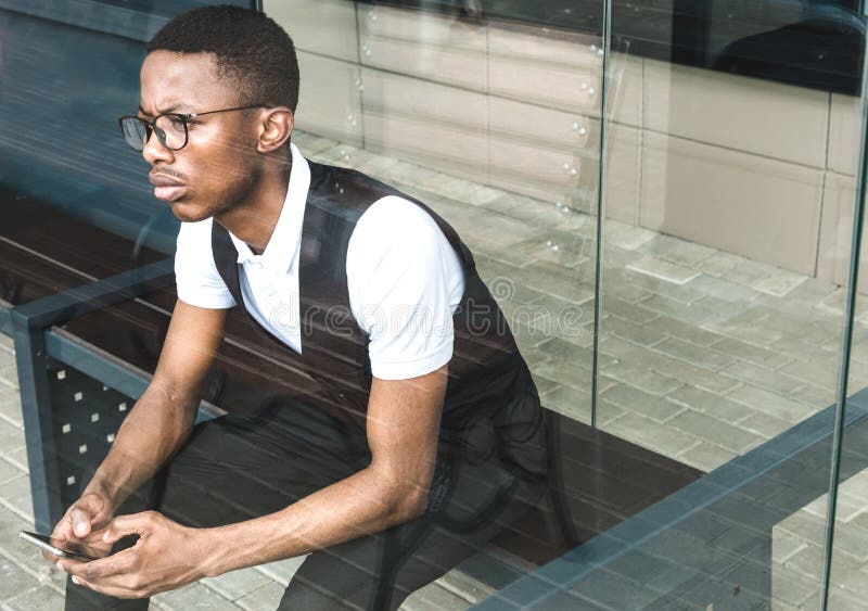 Jeune homme d'affaires d'afro-américain dans le costume et lunettes parlant au téléphone sur le fond du centre d'affaires image libre de droits Jeune homme d'affaires d'afro-américain dans le costume et lunettes parlant au téléphone sur le fond du centre d'affaires image libre de droits