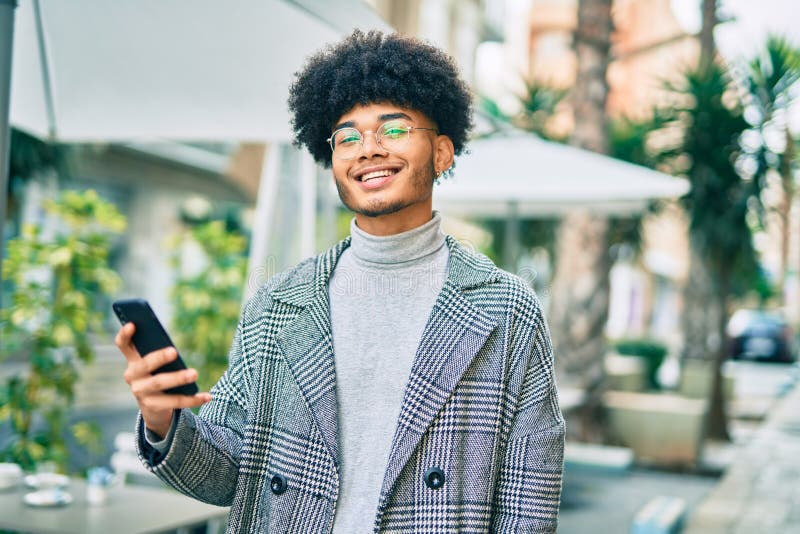 Jeune homme d'affaires afro-américain souriant heureux en utilisant un smartphone à la ville photographie stock
