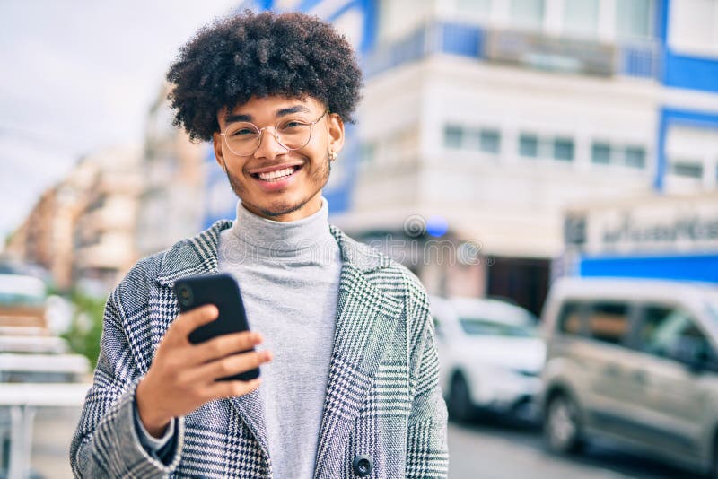 Jeune homme d'affaires afro-américain souriant heureux en utilisant un smartphone à la ville photos libres de droits