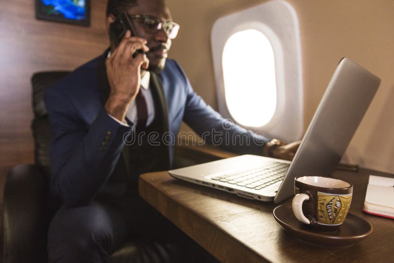 Jeune homme d'affaires attirant et r?ussi d'Afro-am?ricain avec des glassies parlant le t?l?phone et le moment fonctionnant image libre de droits Jeune homme d'affaires attirant et r?ussi d'Afro-am?ricain avec des glassies parlant le t?l?phone et le moment fonctionnant image libre de droits
