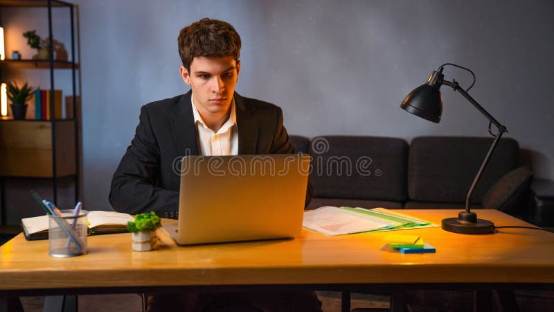 Jeune homme d'affaires dans le bureau travaillant tard le soir homme assis au bureau avec ordinateur portable regardant à l'écran image stock