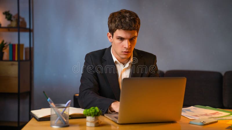 Jeune homme d'affaires dans le bureau travaillant tard le soir homme assis au bureau avec ordinateur portable regardant à l'écran image libre de droits