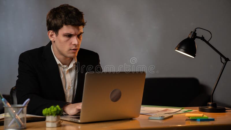 Jeune homme d'affaires dans le bureau travaillant tard le soir homme assis au bureau avec ordinateur portable regardant à l'écran images stock