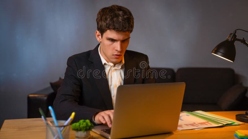 Jeune homme d'affaires dans le bureau travaillant tard le soir homme assis au bureau avec ordinateur portable regardant à l'écran photos stock