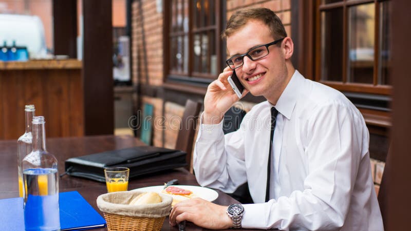Smiling young businessman making a call with his smartphone in a restaurant. Smiling young businessman making a call with his smartphone in a restaurant