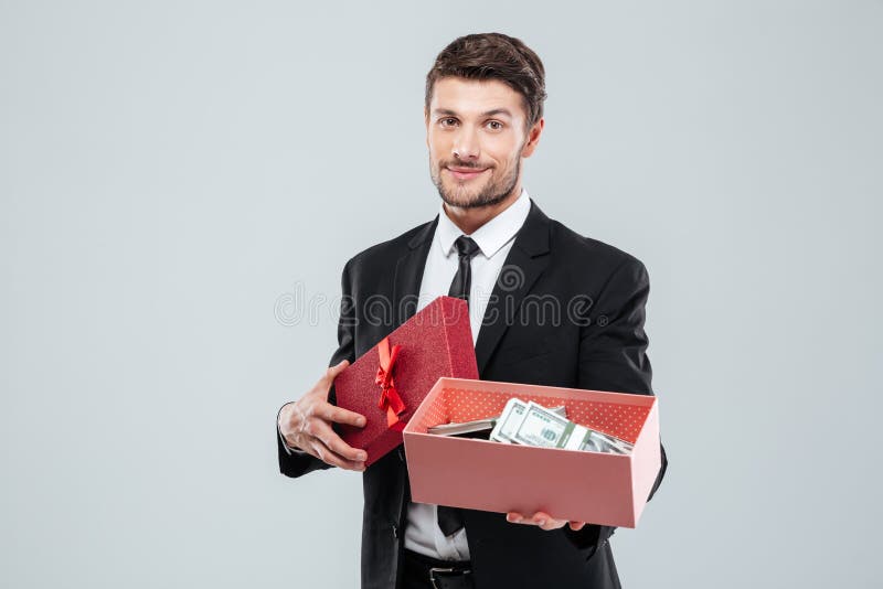 Jeune homme d'affaires de sourire montrant la boîte actuelle complètement d'argent image libre de droits Jeune homme d'affaires de sourire montrant la boîte actuelle complètement d'argent image libre de droits