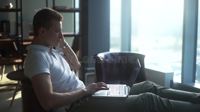 Jeune homme d'affaires pensive à écrire sur un ordinateur portable mettre ses pieds sur une table basse banque de vidéos