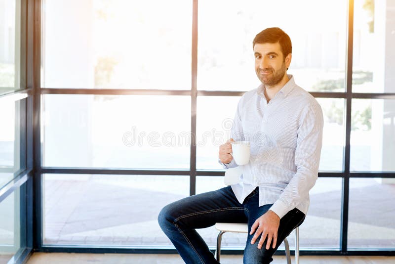 Jeune homme d'affaires s'asseyant sur un tabouret dans le bureau images stock Jeune homme d'affaires s'asseyant sur un tabouret dans le bureau images stock