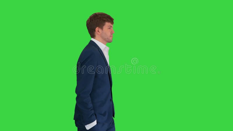 Jeune homme d'affaires sûr marchant avec ses mains dans ses poches sur une clé verte de l'écran chroma. banque de vidéos