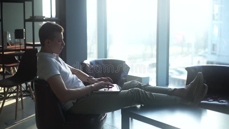 Jeune homme d'affaires sûr à écrire sur un ordinateur portable, mettre ses pieds sur la table basse banque de vidéos