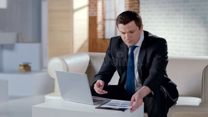 Jeune homme d'affaires vérifiant le rapport financier, travaillant sur l'ordinateur portable dans le bureau moderne photographie stock libre de droits Jeune homme d'affaires vérifiant le rapport financier, travaillant sur l'ordinateur portable dans le bureau moderne photographie stock libre de droits