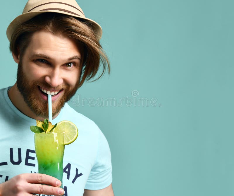 Jeune homme dans l'appareil-photo de regard heureux potable de jus de boissons de cocktail de margarita de chapeau image libre de droits Jeune homme dans l'appareil-photo de regard heureux potable de jus de boissons de cocktail de margarita de chapeau image libre de droits