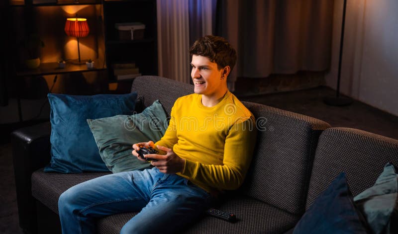Jeune homme dans la soirée après le travail relaxant à la maison assis sur le canapé dans le salon regarder la télévision tient jo photo libre de droits