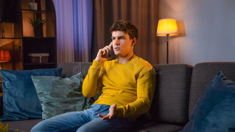 Jeune homme dans la soirée après le travail se détendre à la maison assis sur le canapé dans le salon regarder la télévision et pa images stock