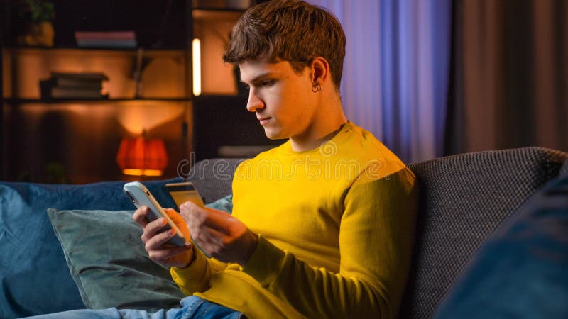 Jeune homme dans la soirée après le travail se détendre à la maison assis sur le canapé dans le salon regarder la télévision taper photo libre de droits