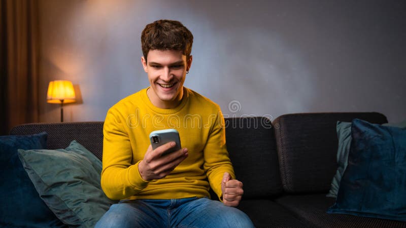 Jeune homme dans la soirée après le travail se détendre à la maison assis sur le canapé dans le salon regarder la vidéo sur le sma image stock