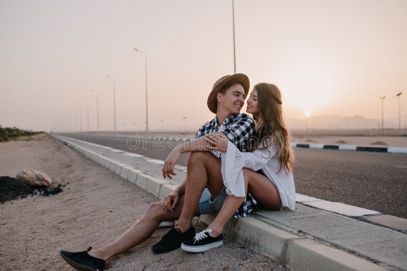 Jeune homme dans le chapeau ? la mode regardant avec amour son amie gracieuse dans la chemise blanche, tout en se reposant apr?s photos stock Jeune homme dans le chapeau ? la mode regardant avec amour son amie gracieuse dans la chemise blanche, tout en se reposant apr?s photos stock