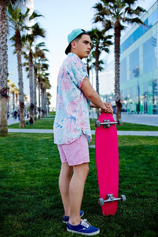 Jeune homme de hippie se tenant sur l'herbe tenant son longboard image stock Jeune homme de hippie se tenant sur l'herbe tenant son longboard image stock