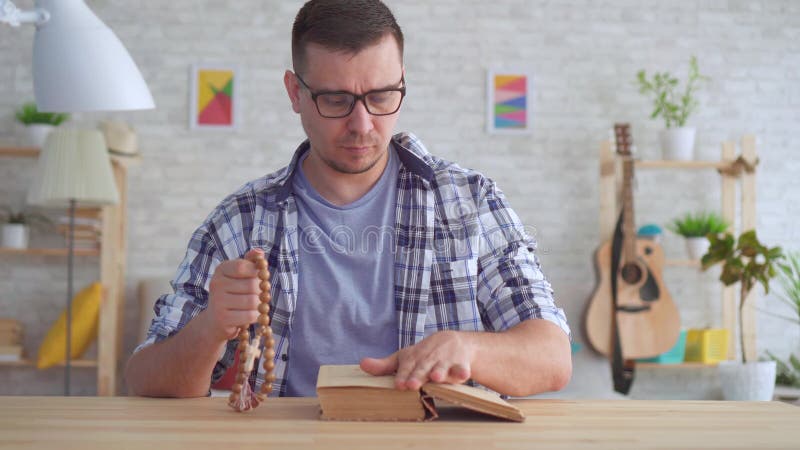 Jeune homme de portrait avec des verres avec un chapelet ses mains et en lisant la bible banque de vidéos