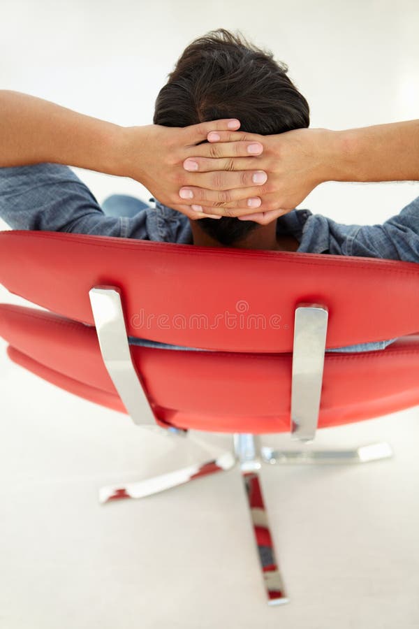 Jeune homme détendant dans la présidence rouge photos stock Jeune homme détendant dans la présidence rouge photos stock