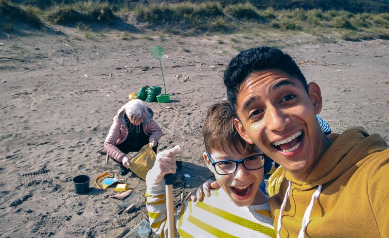 Jeune homme et enfant prenant selfie alors que le groupe de volontaires à nettoyer la plage image libre de droits