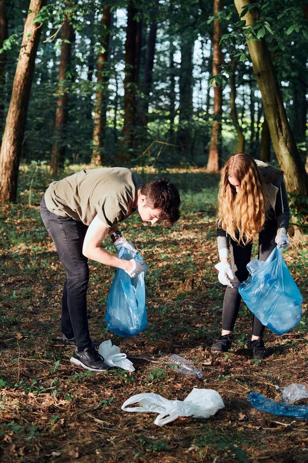 Jeune homme et femme une forêt de nettoyage. Volontaires à cueillir les déchets des sacs en plastique photographie stock libre de droits