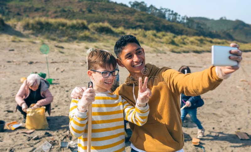 Jeune homme et garçon prenant le selfie à un groupe de bénévoles nettoyer la plage photo libre de droits