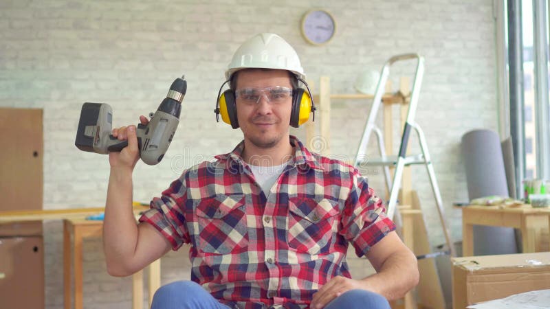 Jeune homme handicapé de portrait dans un fauteuil roulant dans un casque et avec une perceuse électrique dedans sa main banque de vidéos