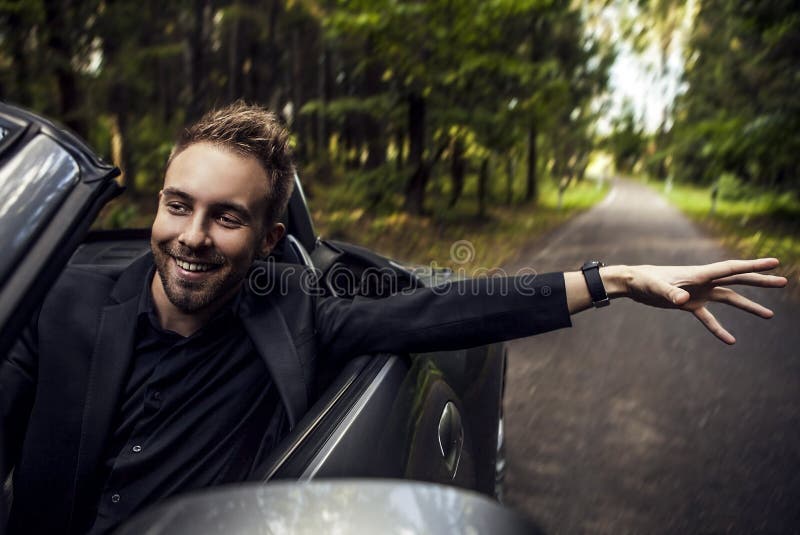 Jeune homme heureux élégant dans la voiture convertible extérieure. image stock Jeune homme heureux élégant dans la voiture convertible extérieure. image stock