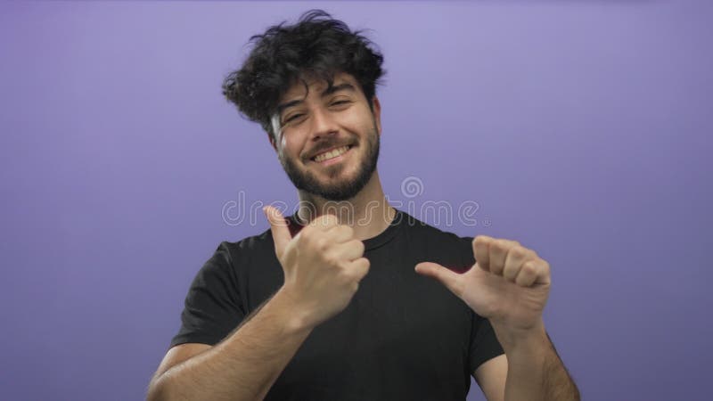 Jeune homme hispanique à la barbe sourit et fait des gestes avec des pouces sur le côté, sur un fond violet plein de vitalité, tra clips vidéos