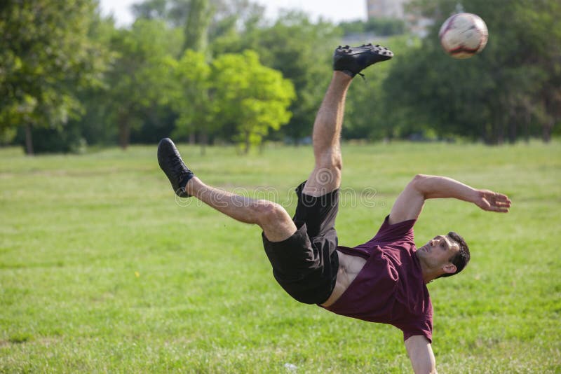 Jeune homme jouant au football en parc maintenant la boule dans l'air photo stock Jeune homme jouant au football en parc maintenant la boule dans l'air photo stock