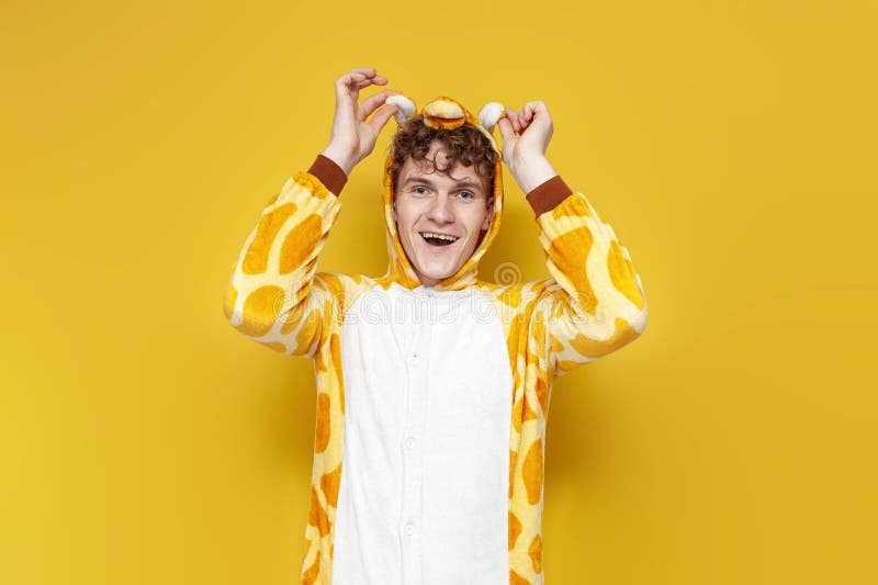 Jeune homme joyeux en drôles pyjamas girafe tient des oreilles sur fond jaune homme en costume animal image libre de droits