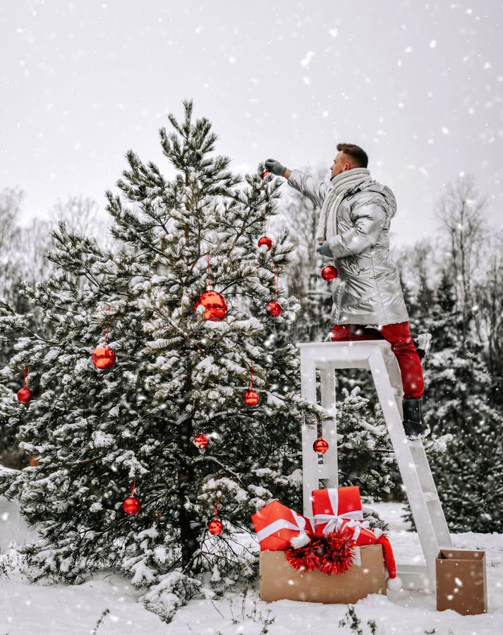 Jeune homme la position d'argent élégante de veste sur les selles et en décorant l'arbre de Noël avec des balles dehors
